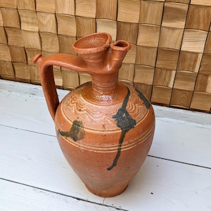 May include: A terracotta pitcher with a brown glaze and a unique spout. The pitcher has a carved design and is decorated with blue and green accents.