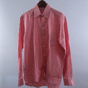 May include: A long-sleeve button-down shirt featuring a red and white checkered pattern. The shirt has a pointed collar, a full-length front button placket, and buttoned cuffs. The fabric displays a consistent grid design throughout the garment.