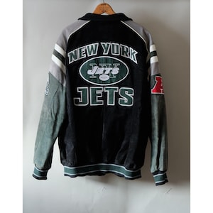 Puede incluir: Una chaqueta universitaria de los New York Jets en negro, gris y verde con logotipos y texto del equipo bordados en la espalda. La chaqueta tiene mangas largas con rayas blancas, cuello acanalado y puños acanalados. La espalda muestra el texto New York Jets.