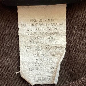 May include: A white care label with black text detailing washing instructions for a garment. The text reads "Pre-shrunk, Machine wash warm, Do not bleach, Tumble dry low, Do not iron, Decorated, 100% Cotton, RN 38327, Made in Mexico, Large."