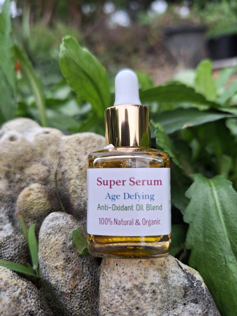 May include: A small glass bottle with a gold cap and a white dropper. The bottle contains a yellow liquid and has a label that reads "Super Serum Age Defying Anti-Oxidant Oil Blend 100% Natural & Organic".