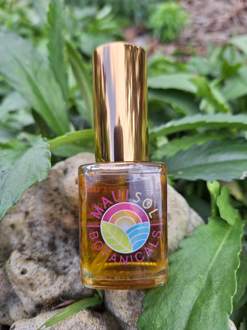 May include: A small, clear glass bottle with a gold cap. The bottle contains a golden liquid and has a label with the text "Maui Sol Botanicals" and a colorful logo of a sun, waves, and a leaf.