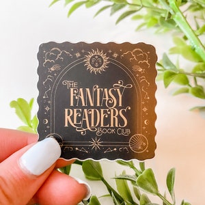 K&ouml;nnte beinhalten: Ein schwarzer Aufkleber mit goldenem Design, das einen Halbmond, Sterne und eine Sonne mit einem Gesicht zeigt. Der Text "The Fantasy Readers Book Club" ist in einer dekorativen Schrift geschrieben.