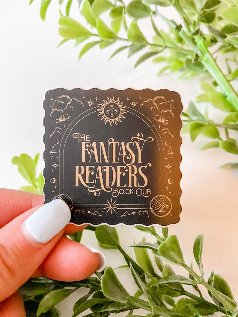 K&ouml;nnte beinhalten: Ein schwarzer Aufkleber mit goldenem Design, das einen Halbmond, Sterne und eine Sonne mit einem Gesicht zeigt. Der Text "The Fantasy Readers Book Club" ist in einer dekorativen Schrift geschrieben.