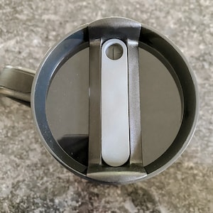 Puede incluir: Taza de viaje negra con tapa deslizante gris. La tapa tiene un peque&ntilde;o agujero para sorber.