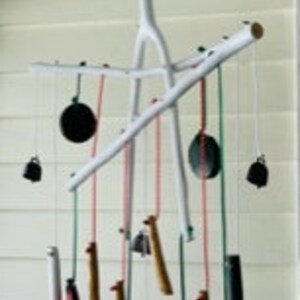 May include: A white wooden wind chime with multiple hanging elements, including bells, wooden beads, and metal discs. The chime is suspended from a white ceiling.