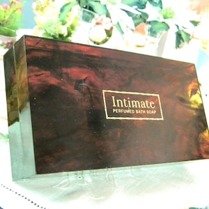 May include: A rectangular box of "Intimate Perfumed Bath Soap" with a dark, marbled pattern. The box has a gold label with the product name. The box is on a white surface.