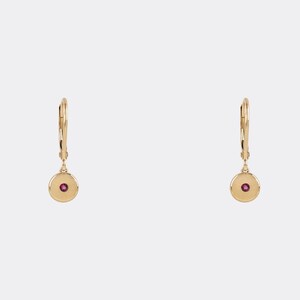 May include: A pair of gold hoop earrings with a small red gemstone in the centre of each hoop.
