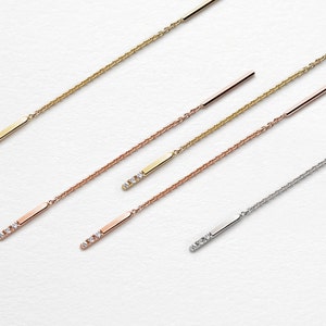 May include: Four delicate gold chains with small diamond accents hanging from a bar. The chains are in different lengths and are shown against a white background.
