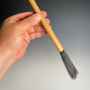 May include: A wooden-handled brush with a black bristle head. The brush has a metal hook at the top of the handle.