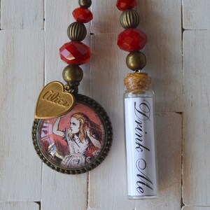 May include: Two Alice in Wonderland-themed charms. One is a round pendant with a picture of Alice and the word "Alice" on a heart-shaped charm. The other is a small glass bottle with the words "Drink Me". Both have red and gold bead accents.