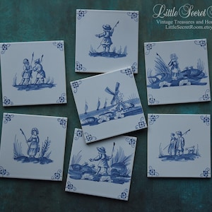Può includere: Una collezione di sette piastrelle quadrate in ceramica con illustrazioni blu e bianche. Ogni piastrella presenta una scena pastorale diversa, tra cui figure con canne da pesca e un mulino a vento. Le piastrelle hanno accenti decorativi.
