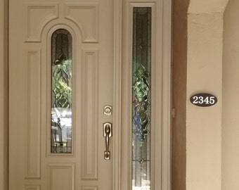 Könnte beinhalten: Eine weiße Haustür mit einem Glaseinsatz und einem Messing-Türgriff. Die Tür hat ein kleines Fenster mit einem dekorativen Glasmuster. Die Hausnummer 2345 ist an der Wand rechts neben der Tür zu sehen.