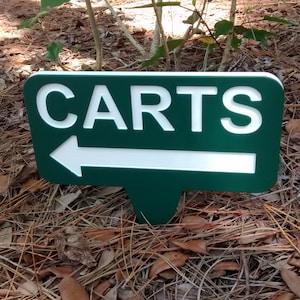 Puede incluir: Un letrero verde con letras blancas y una flecha blanca que apunta hacia la izquierda. El letrero dice "CARTS".