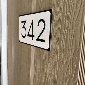 Pode incluir: Uma placa de n&uacute;mero de casa retangular branca com moldura preta e n&uacute;meros pretos. A placa diz "342".