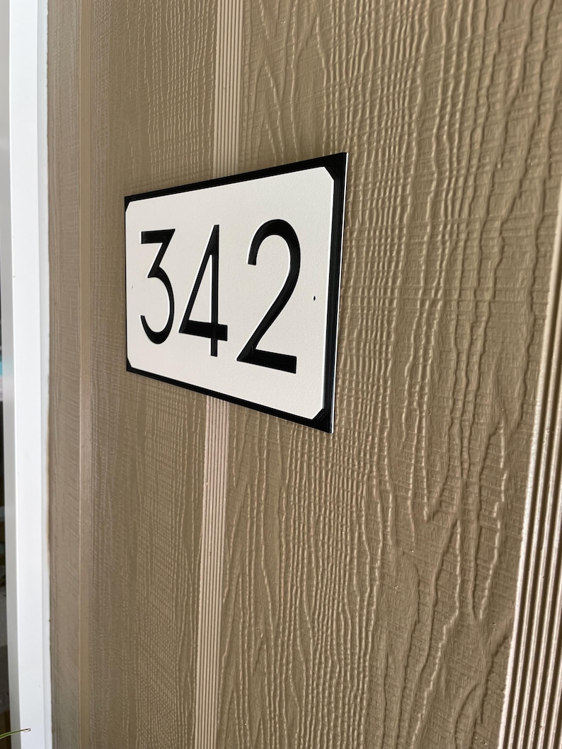 Pode incluir: Uma placa de n&uacute;mero de casa retangular branca com moldura preta e n&uacute;meros pretos. A placa diz "342".