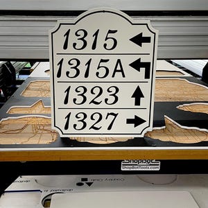 May include: A white sign with black numbers and arrows. The numbers are 1315, 1315A, 1323, and 1327. The arrows point left, right, up, and right.