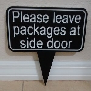 May include: Black sign with white lettering that reads "Please leave packages at side door".