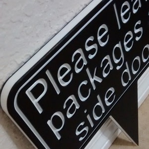 May include: Black and white sign with a speech bubble shape that says "Please leave packages side door".