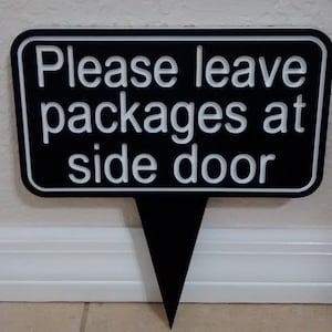 May include: Black sign with white text that reads "Please leave packages at side door".