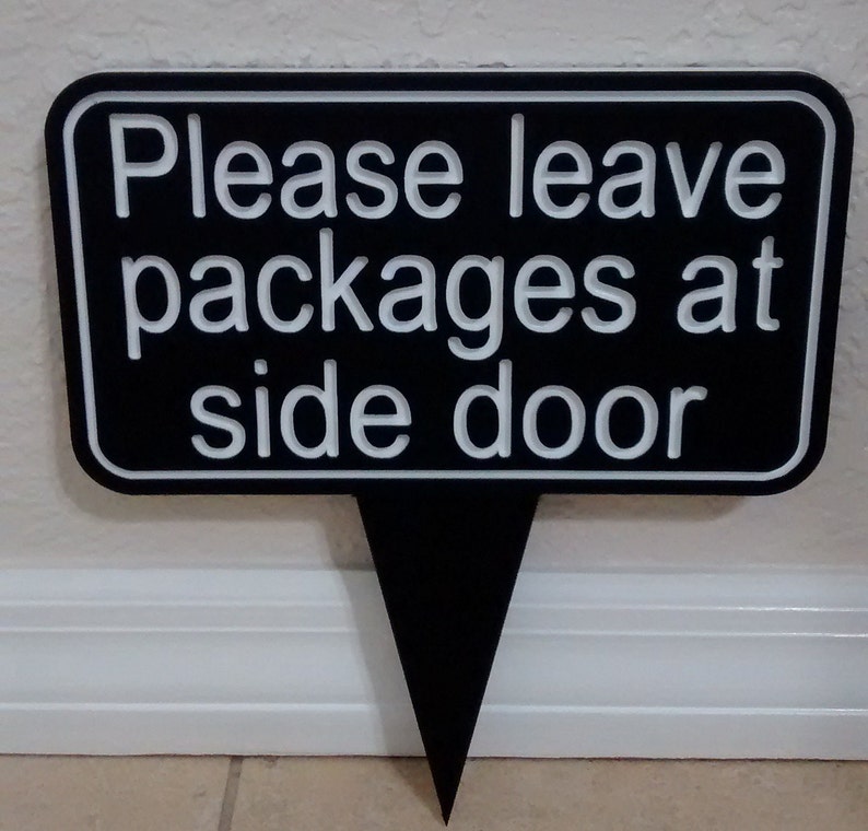 May include: Black sign with white text that reads "Please leave packages at side door".