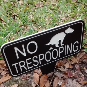 Op de afbeelding: Een zwart-wit bord met een wit silhouet van een hond die poept en de tekst "NO TRESPOOPING".