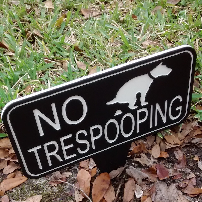 Op de afbeelding: Een zwart-wit bord met een wit silhouet van een hond die poept en de tekst "NO TRESPOOPING".
