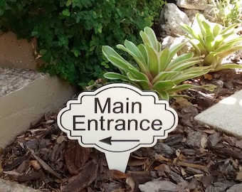 May include: White sign with black text and an arrow pointing to the right. The sign reads "Main Entrance".