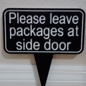 May include: Black sign with white text that reads "Please leave packages at side door".