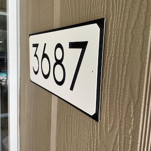 Pode incluir: Uma placa de n&uacute;mero de casa retangular branca com moldura preta e n&uacute;meros pretos. A placa diz "3687".