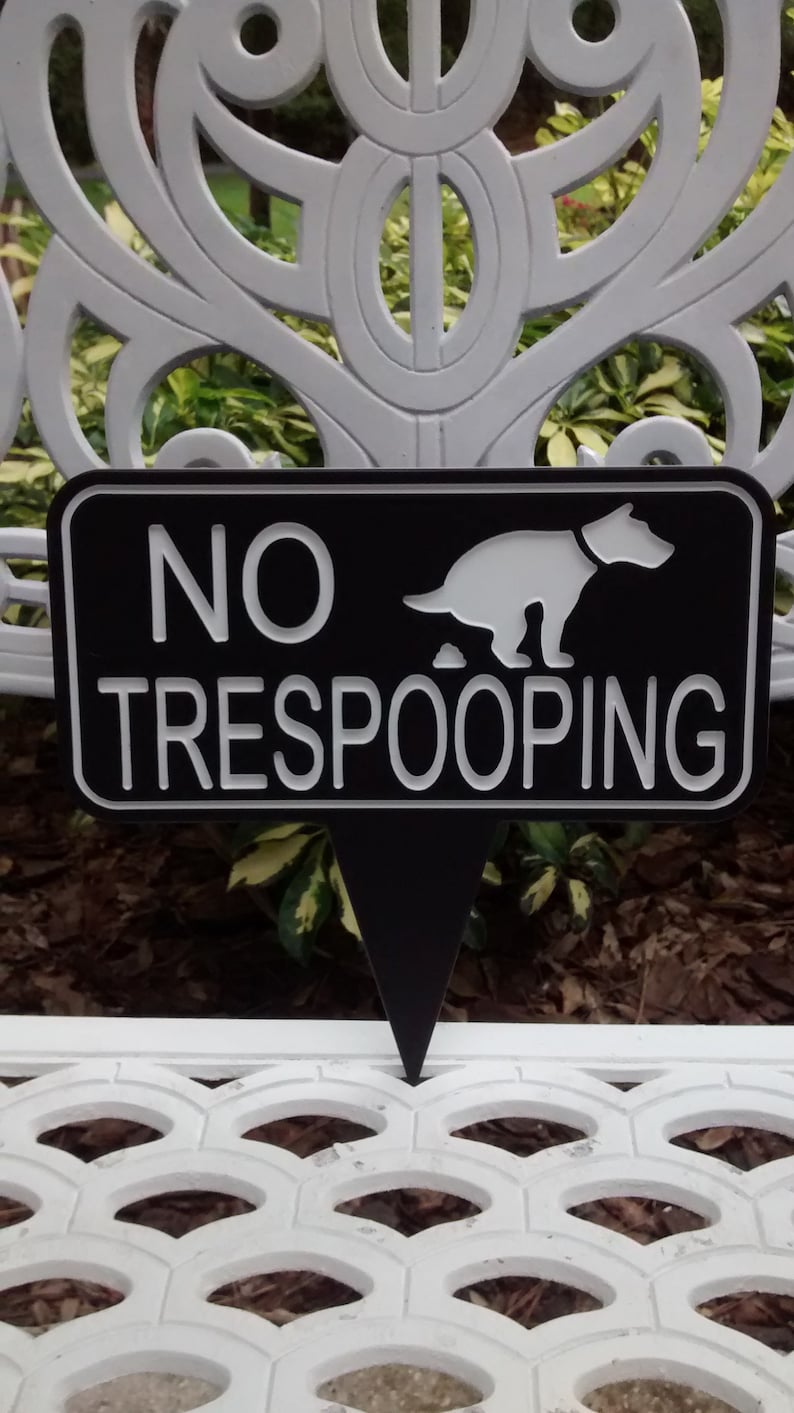 Op de afbeelding: Een zwart-wit bord met de tekst "NO TRESPOOPING" en een wit silhouet van een hond die poept. Het bord is gevormd als een puntige pijl.