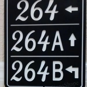 May include: Black and white house number sign with three lines of text. The top line reads "264" with an arrow pointing left. The middle line reads "264A" with an arrow pointing up. The bottom line reads "264B" with an arrow pointing left.