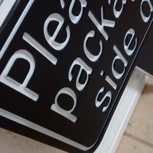 May include: Black sign with white lettering that reads "Please pack on side of cart". The sign is on a white stand.