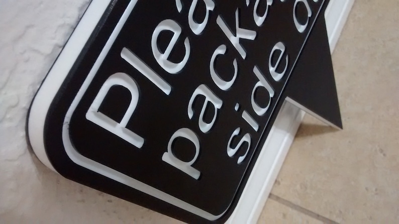 May include: Black sign with white lettering that reads "Please pack on side of cart". The sign is on a white stand.