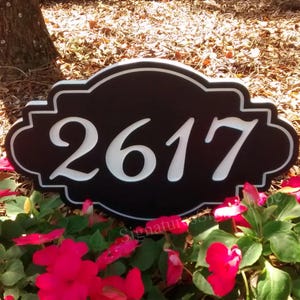 May include: Black and white house number sign with the number 2617 in white on a black background. The sign is in a decorative, ornate style and is surrounded by red flowers.
