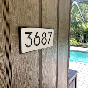 Pode incluir: Uma placa de n&uacute;mero de casa retangular branca com moldura preta e o n&uacute;mero 3687 impresso em preto.