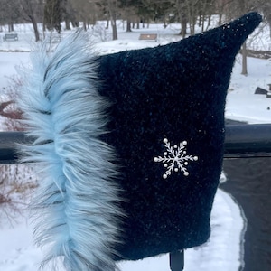 May include: A black and blue winter hat with a white faux fur trim and a snowflake embellishment. The hat is on a pair of walking poles.