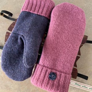 以下が含まれることがあります： ダークチャコールグレーのミトンとダスティローズピンクのミトンがペアになったニットミトン。どちらのミトンにもリブ編みのカフスが付いており、ピンクのミトンには手首部分にダークカラーの丸いボタンが1つあしらわれています。
