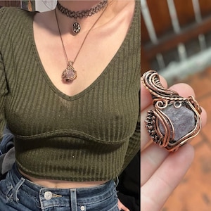 Puede incluir: Un colgante de alambre de cobre envuelto alrededor de una gran piedra preciosa de color púrpura claro de forma irregular. El colgante está colgado de una cadena de plata con un pequeño colgante circular.