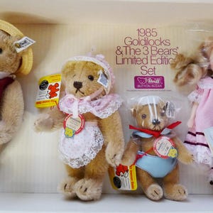 May include: A boxed set of Steiff collectible toys, including three teddy bears and a doll. The bears are dressed in various outfits, including a hat, scarf, and bonnet. The doll wears a pink dress. The box reads "1985 Goldilocks & The 3 Bears Limited Edition Set."