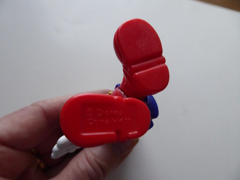 K&ouml;nnte beinhalten: Nahaufnahme eines roten Schuhs einer Disney-Figur. Die Sohle des Schuhs hat ein strukturiertes Design. Die Figur weist auch blaue und wei&szlig;e Elemente auf. Der Text "&copy; Disney China HK" ist auf der Sohle sichtbar.