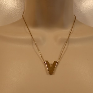Peut inclure: Un collier en chaîne dorée avec un pendentif en forme de lettre V dorée.