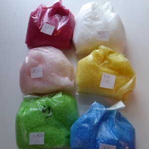 May include: Six bags of colorful beads, each bag labeled with a weight in ounces. The bags are red, white, pink, yellow, green, and blue.