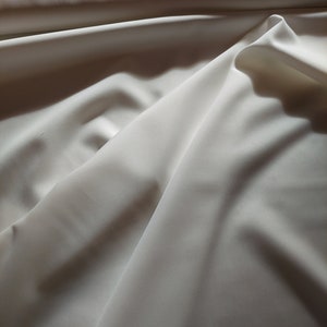 May include: White fabric with soft folds and wrinkles, creating a smooth, flowing texture.