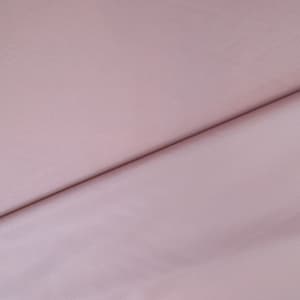 May include: A close-up shot of a light mauve fabric. The fabric is folded, creating a diagonal line across the image. The material appears soft and smooth, with subtle variations in tone.