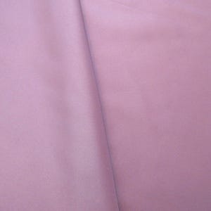 May include: A close-up shot of a solid, light purple fabric. The fabric is smooth and appears to be a lightweight material, with subtle folds and shadows adding depth. The color is consistent throughout the image.