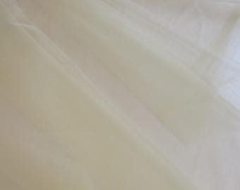 Può includere: Tessuto di tulle bianco sporco, parzialmente arrotolato, con morbide pieghe e un aspetto traslucido. Il tessuto ha una trama delicata e una lucentezza sottile, adatto a vari progetti di artigianato e design.