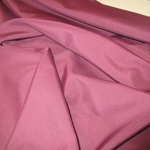 May include: A close-up of a smooth, burgundy fabric. The fabric is folded and draped, showing its texture and colour.