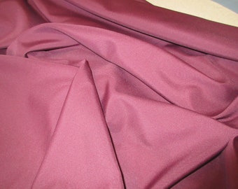 May include: A close-up of a smooth, burgundy fabric. The fabric is folded and draped, showing its texture and color.