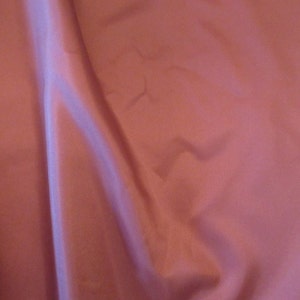 May include: A smooth, pink fabric with a slight sheen. The fabric is folded and draped, creating soft folds and curves.